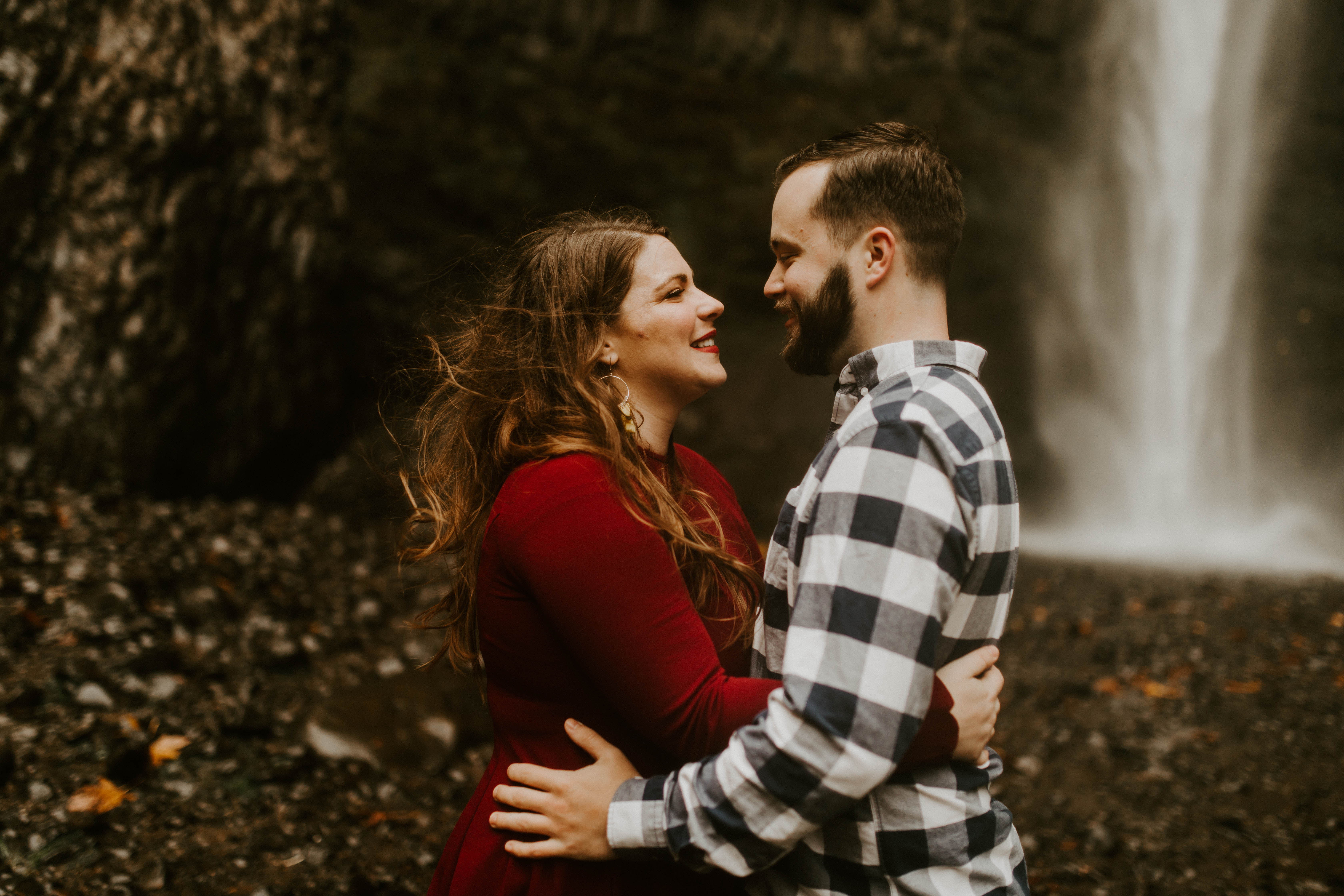 Allison and Brandon looking at each other in front of the waterfall at Latourell Falls. Engagement shoot by Sienna Plus Josh.