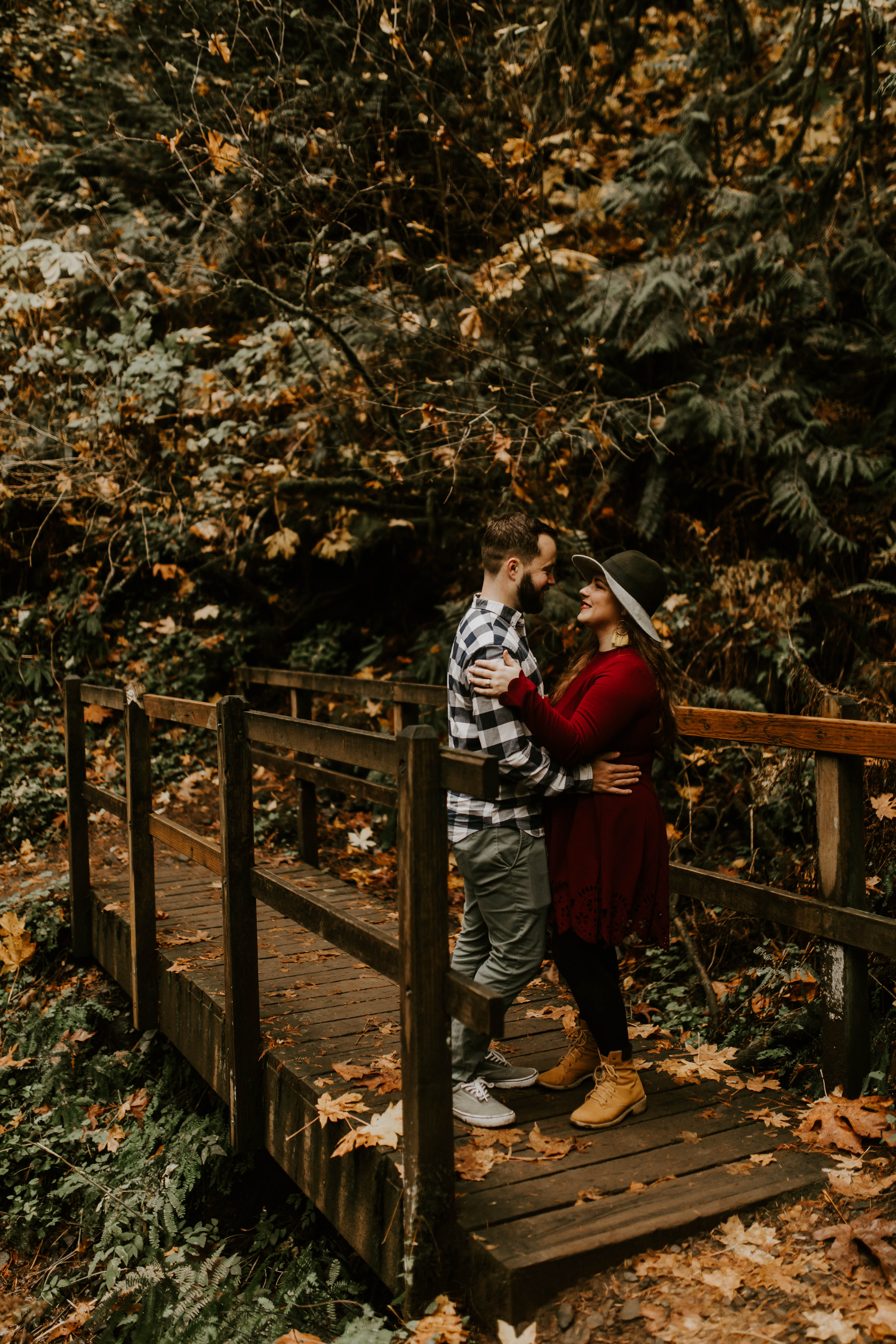Allison and Brandon stand on a bridge, smiling. Engagement shoot by Sienna Plus Josh.