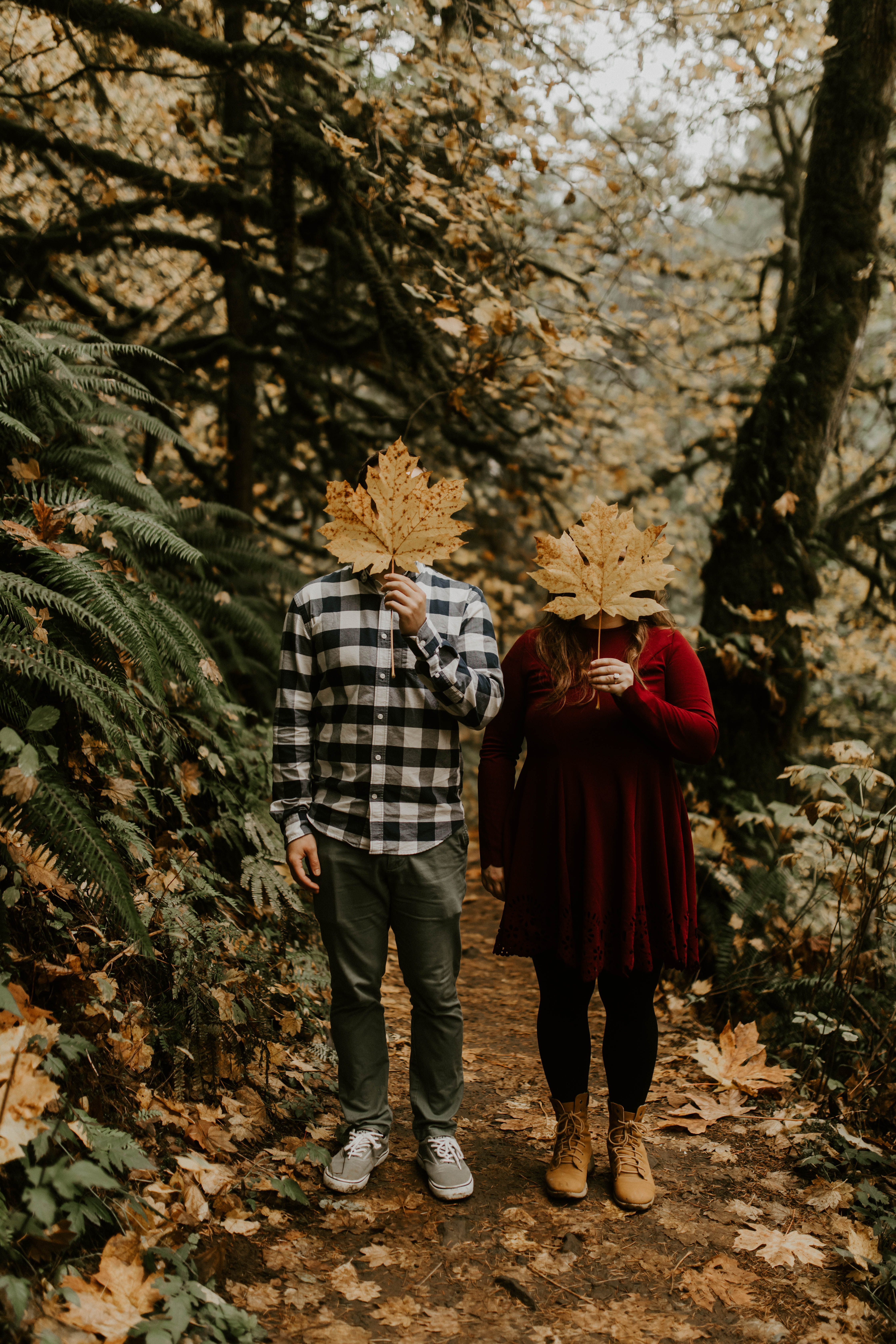 Allison and Brandon cover their faces with leaves at Latourell Falls. Engagement shoot by Sienna Plus Josh.