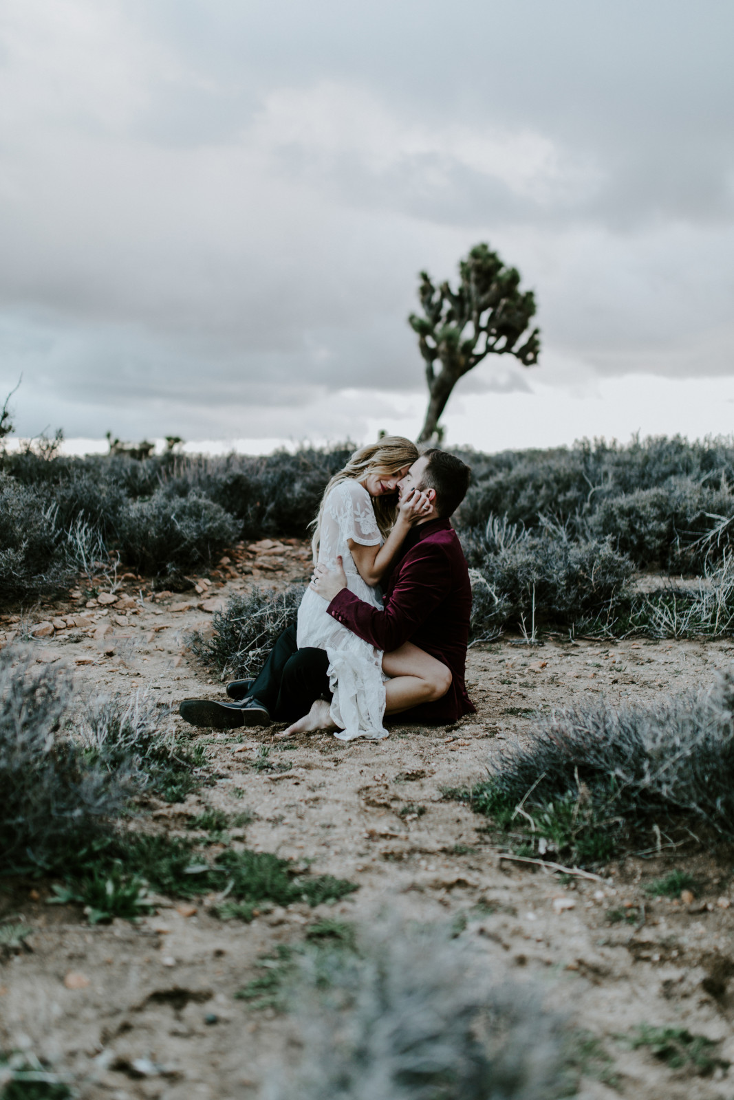 Alyssa and Jeremy kiss as they sit on the sand at Joshua Tree. Elopement wedding photography at Joshua Tree National Park by Sienna Plus Josh.