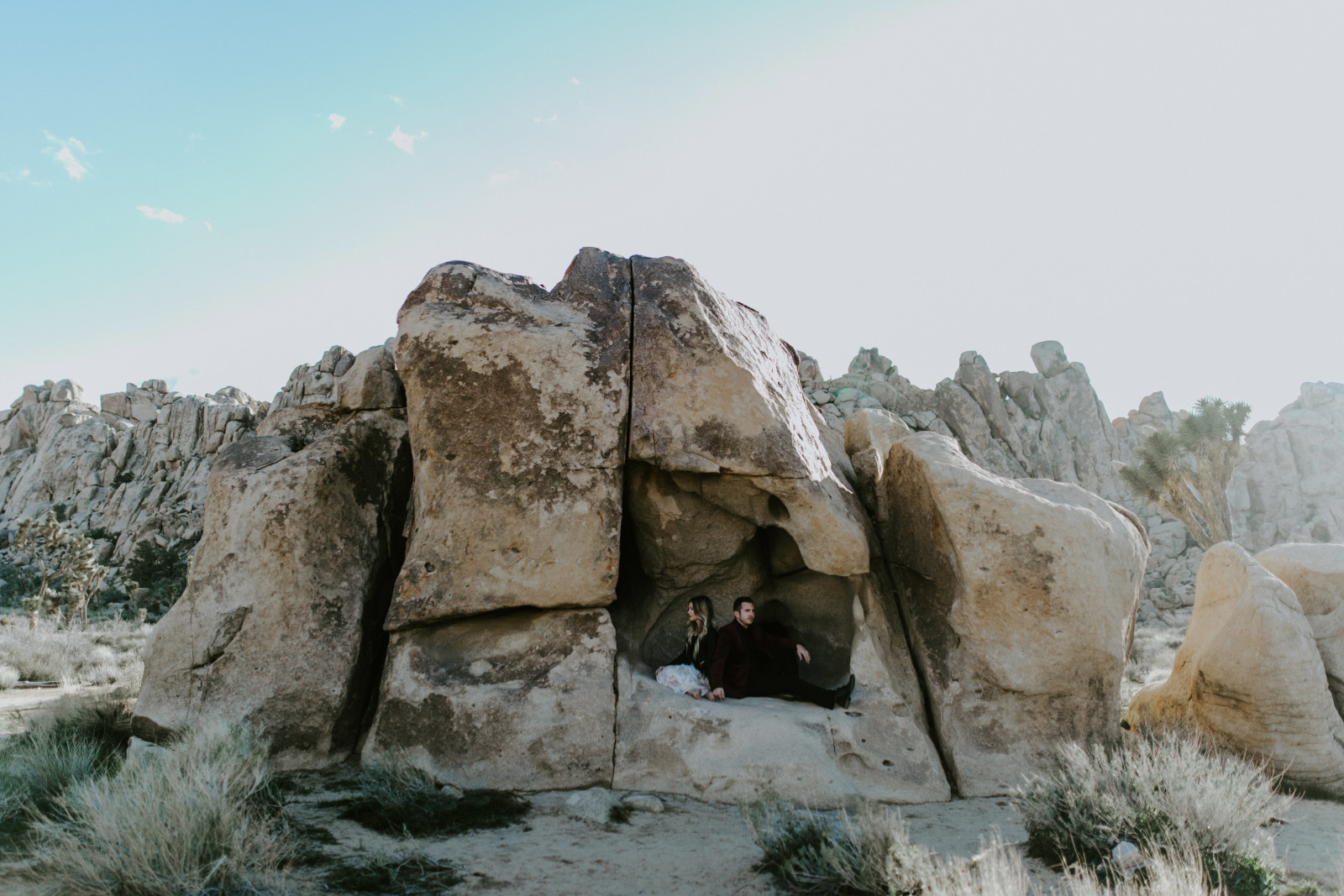 Alyssa and Jeremy sit in a rock formation at Joshua Tree National Park, California. Elopement photography by Sienna Plus Josh.