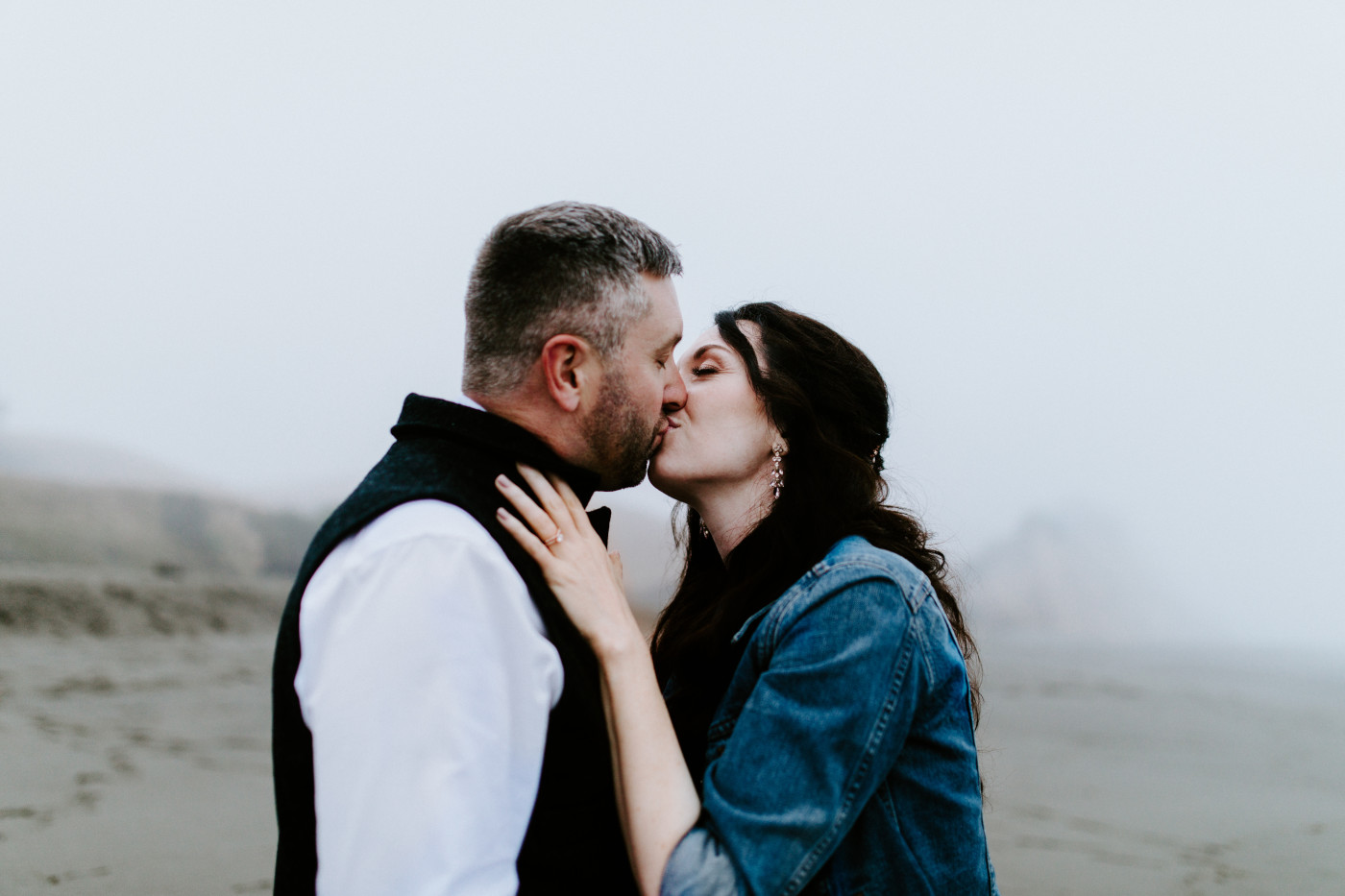 Hannah and Tim kiss on the shoreline.