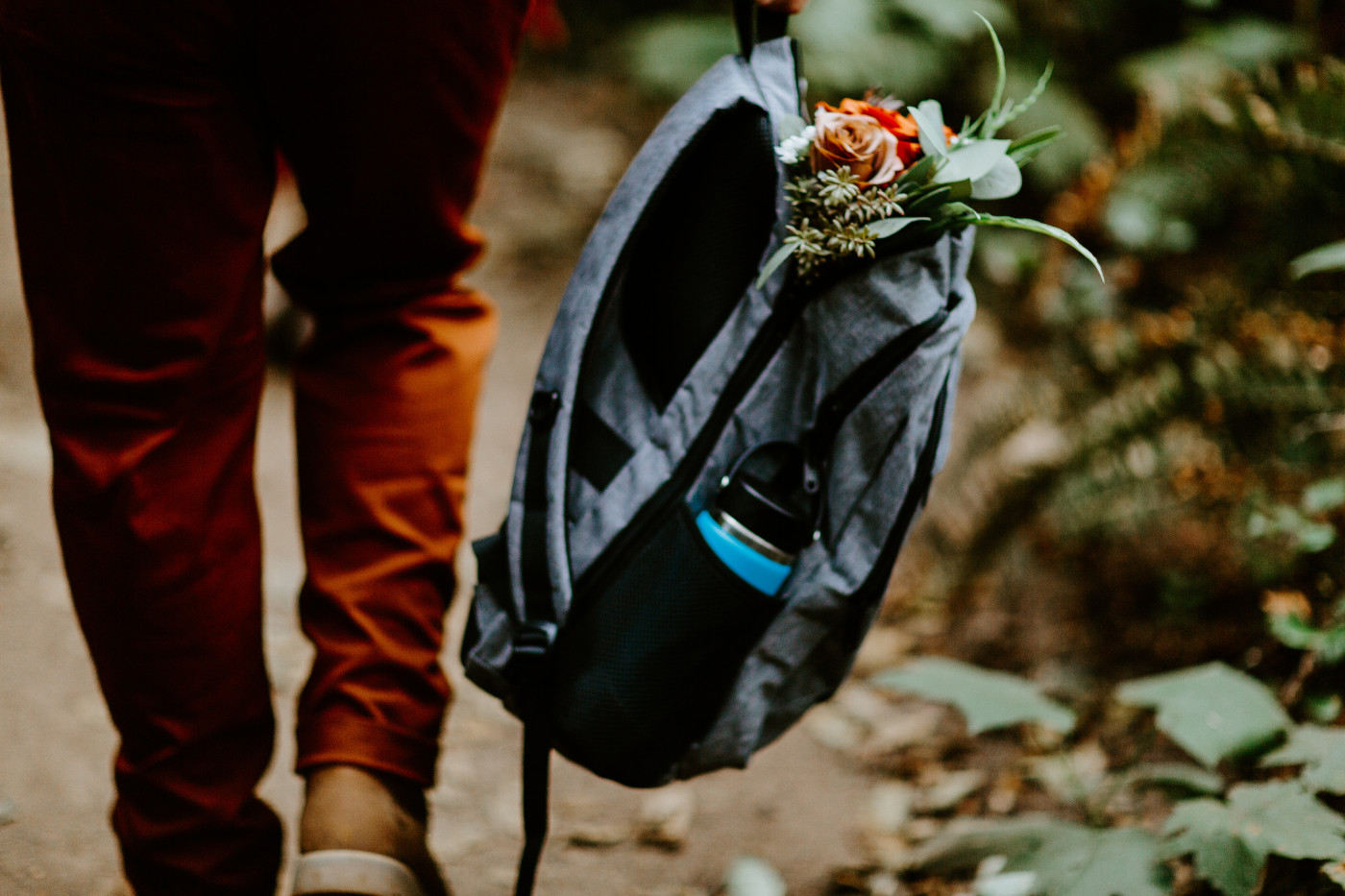 TJ holds his backpack with the bouquet as he hikes to his elopement ceremony spot.