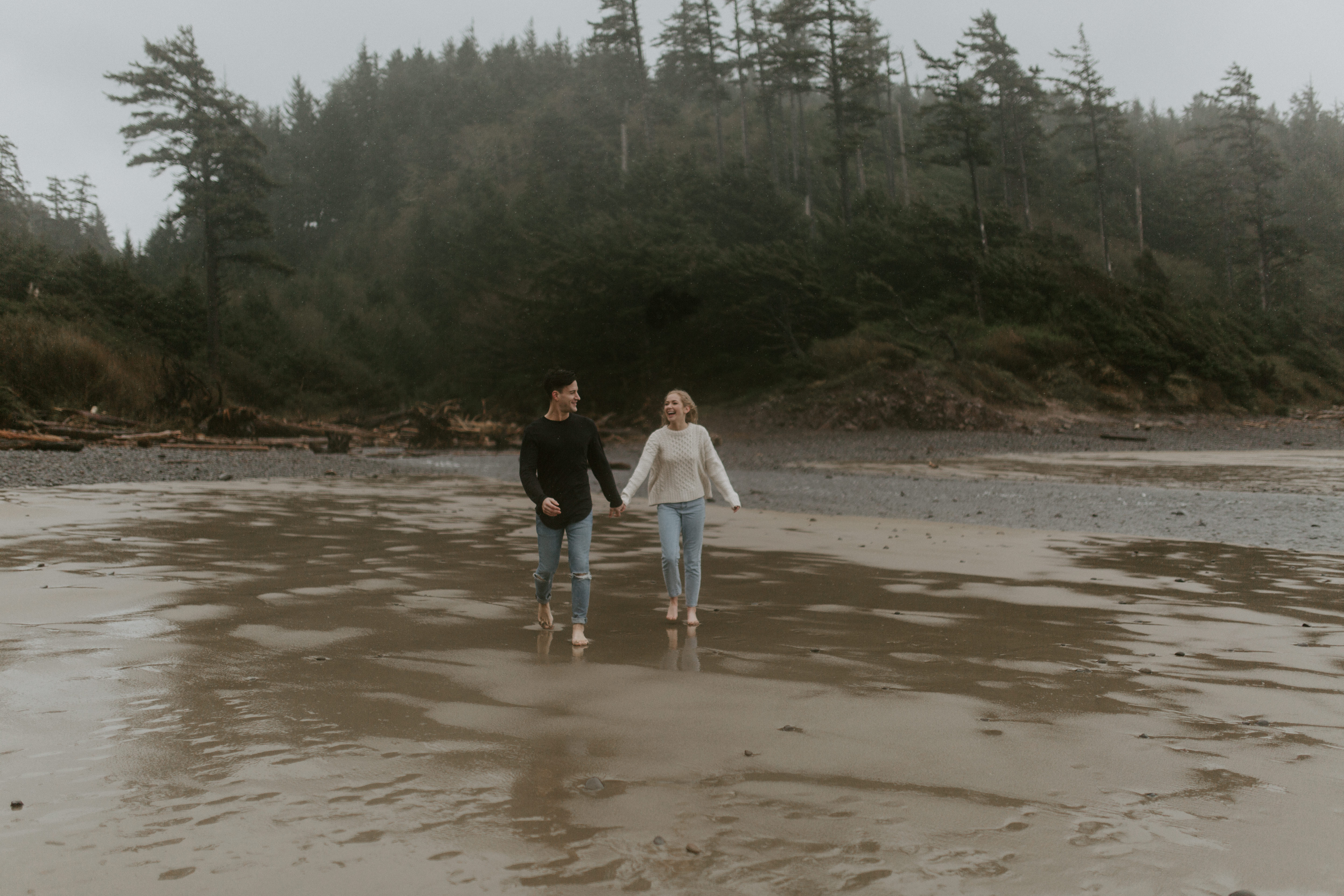 Hannah and Grant hold hands and walk along Indian Beach in Ecola State Park, Oregon. Engagement photography in Oregon by Sienna Plus Josh.