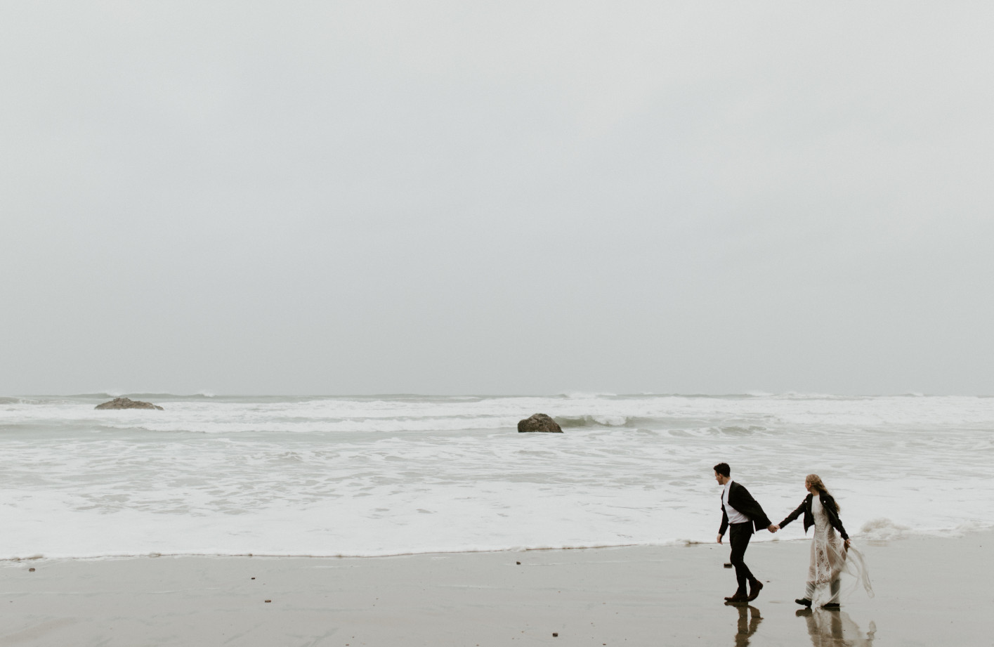 Hannah and Grant walk hand in hand on the sandy shore of Cannon Beach, Oregon. Wedding photography in Portland Oregon by Sienna Plus Josh.