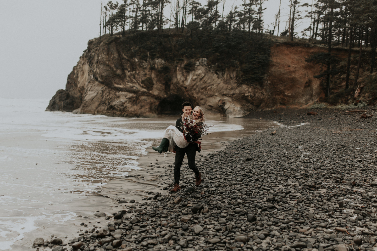 Grant carries Hannah along Cannon Beach in Oregon. Wedding photography in Portland Oregon by Sienna Plus Josh.