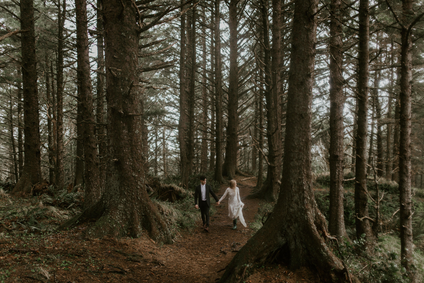 Hannah and Grant walk along the path in the woods at Cannon Beach, Oregon. Wedding photography in Portland Oregon by Sienna Plus Josh.