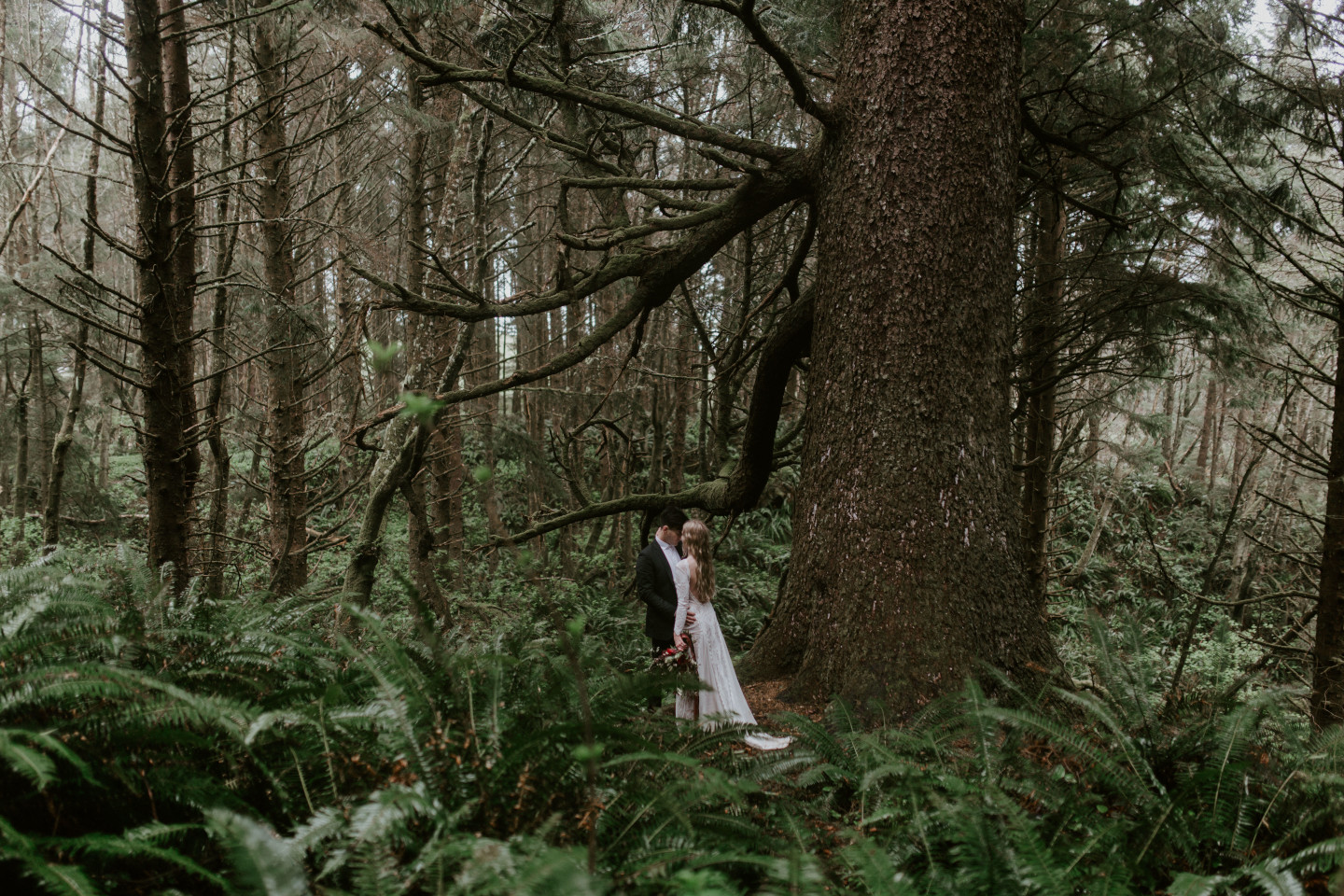 Hannah and Grant stand next to a tree in Cannon Beach, Oregon for their Oregon coast elopement. Wedding photography in Portland Oregon by Sienna Plus Josh.
