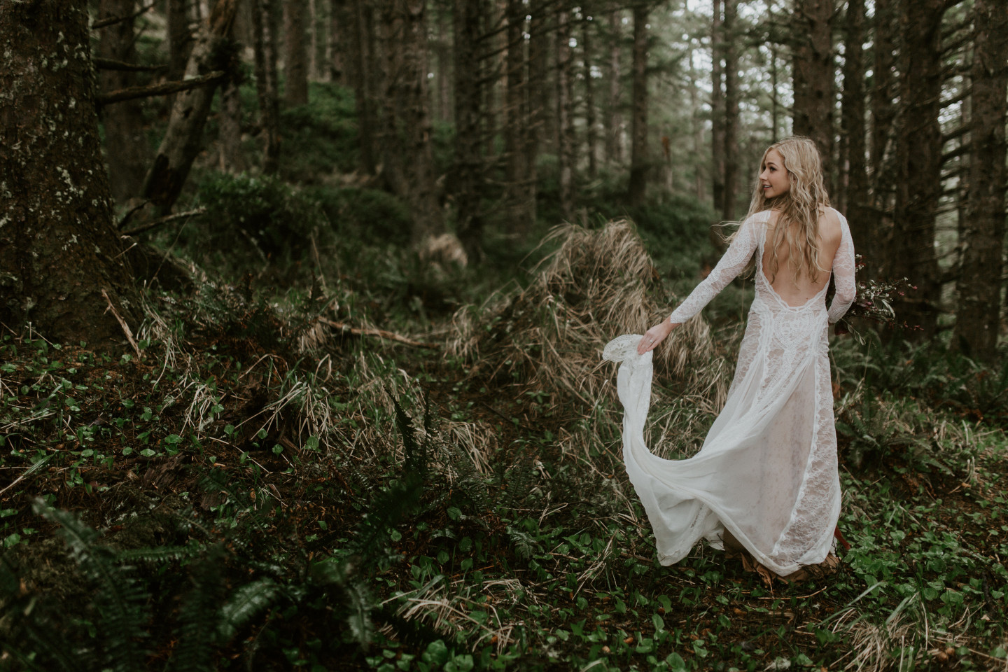 Hannah moves her dress as she walks through the woods in Cannon Beach, Oregon during her Oregon coast elopement. Wedding photography in Portland Oregon by Sienna Plus Josh.