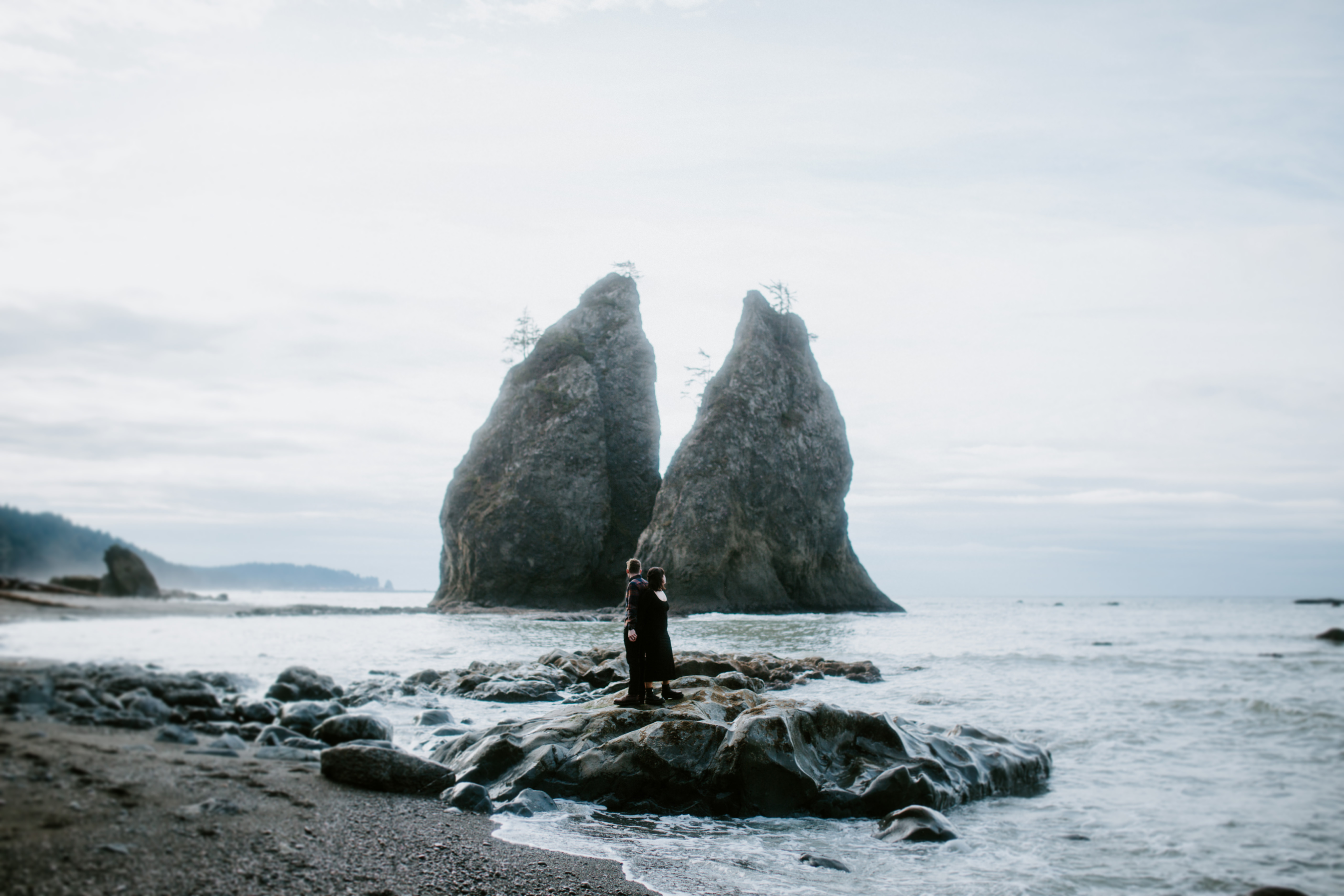 Brett and Bethany stand back to back on a rock at Rialto Beach, Washington.
