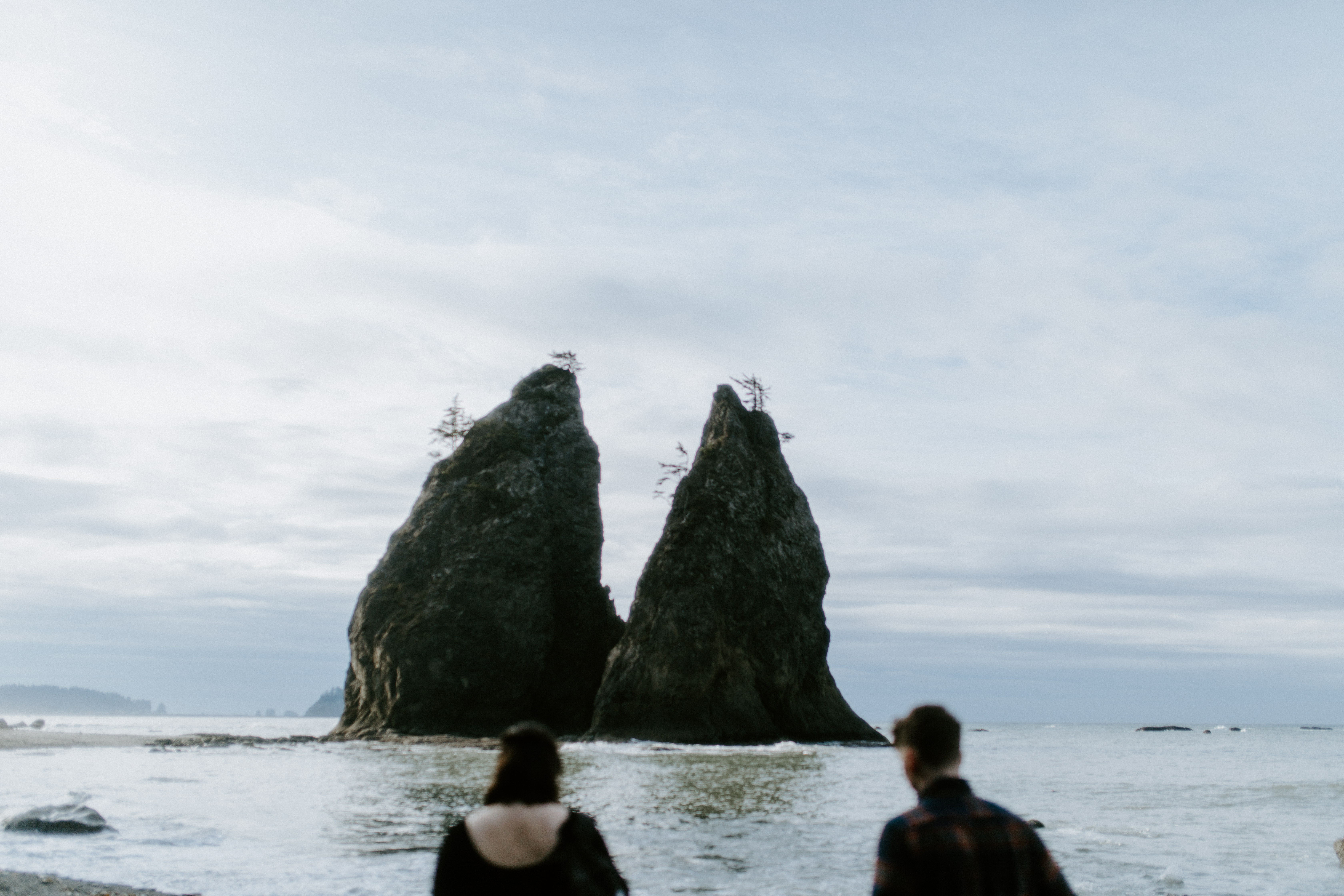Bethany and Brett walk on Rialto Beach toward rocks in the water.