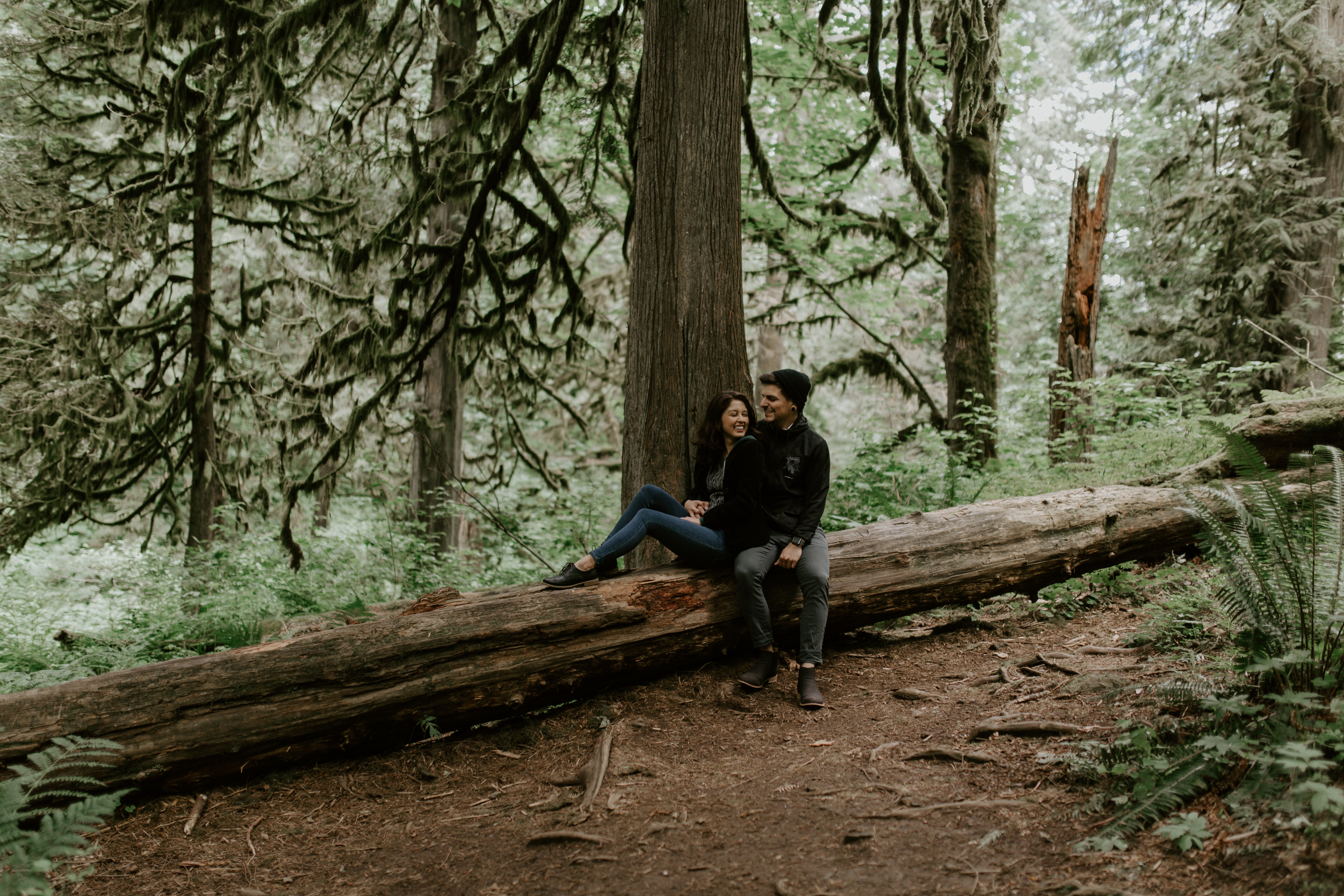 Jasmine and Chris sit on a downed tree at Latourell Falls, Oregon. Adventure photography in Portland Oregon by Sienna Plus Josh.