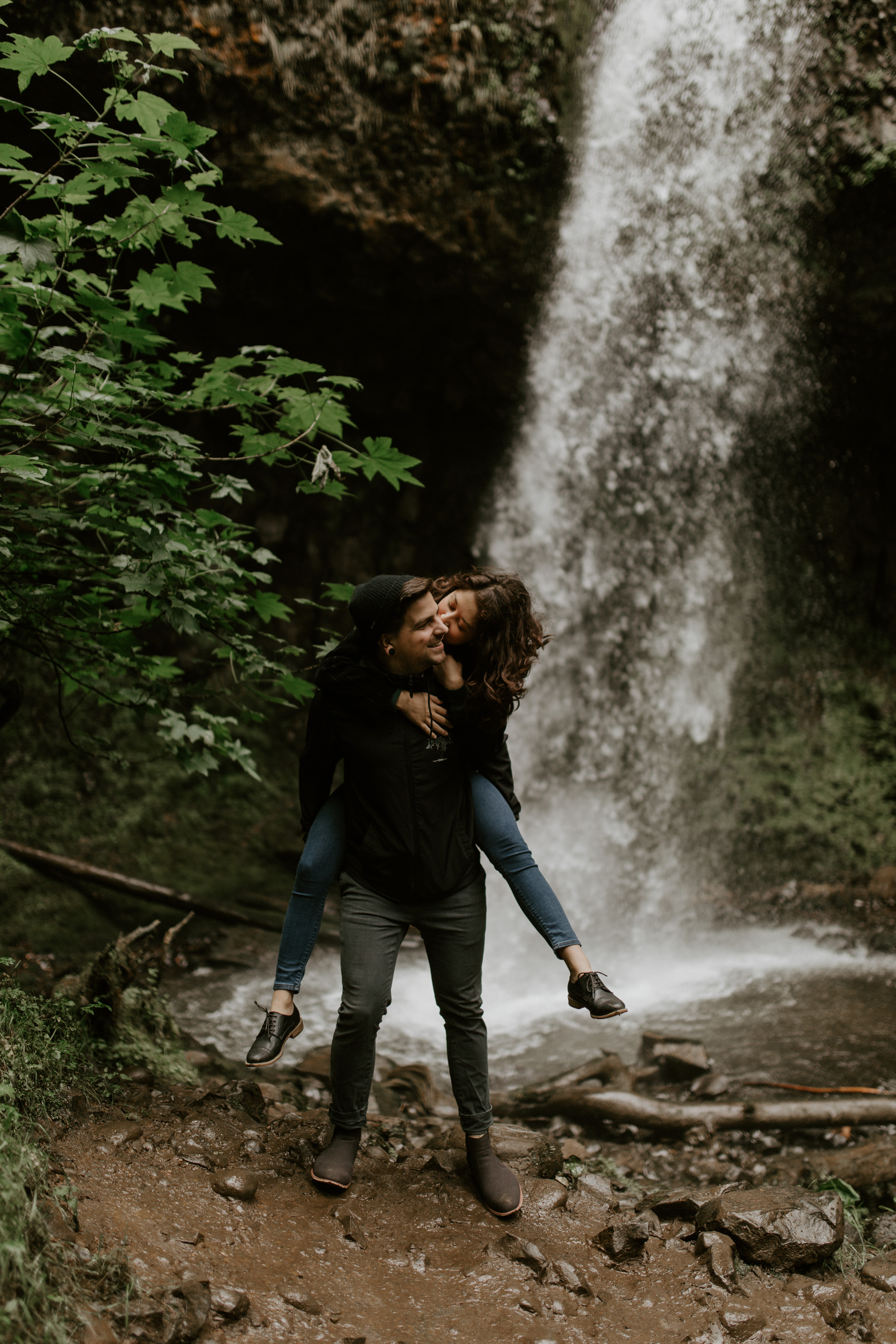 Chris gives Jasmine a piggy back ride while she kisses Chris' cheek at Latourell Falls, Oregon during their Oregon Adventure. Adventure photography in Portland Oregon by Sienna Plus Josh.