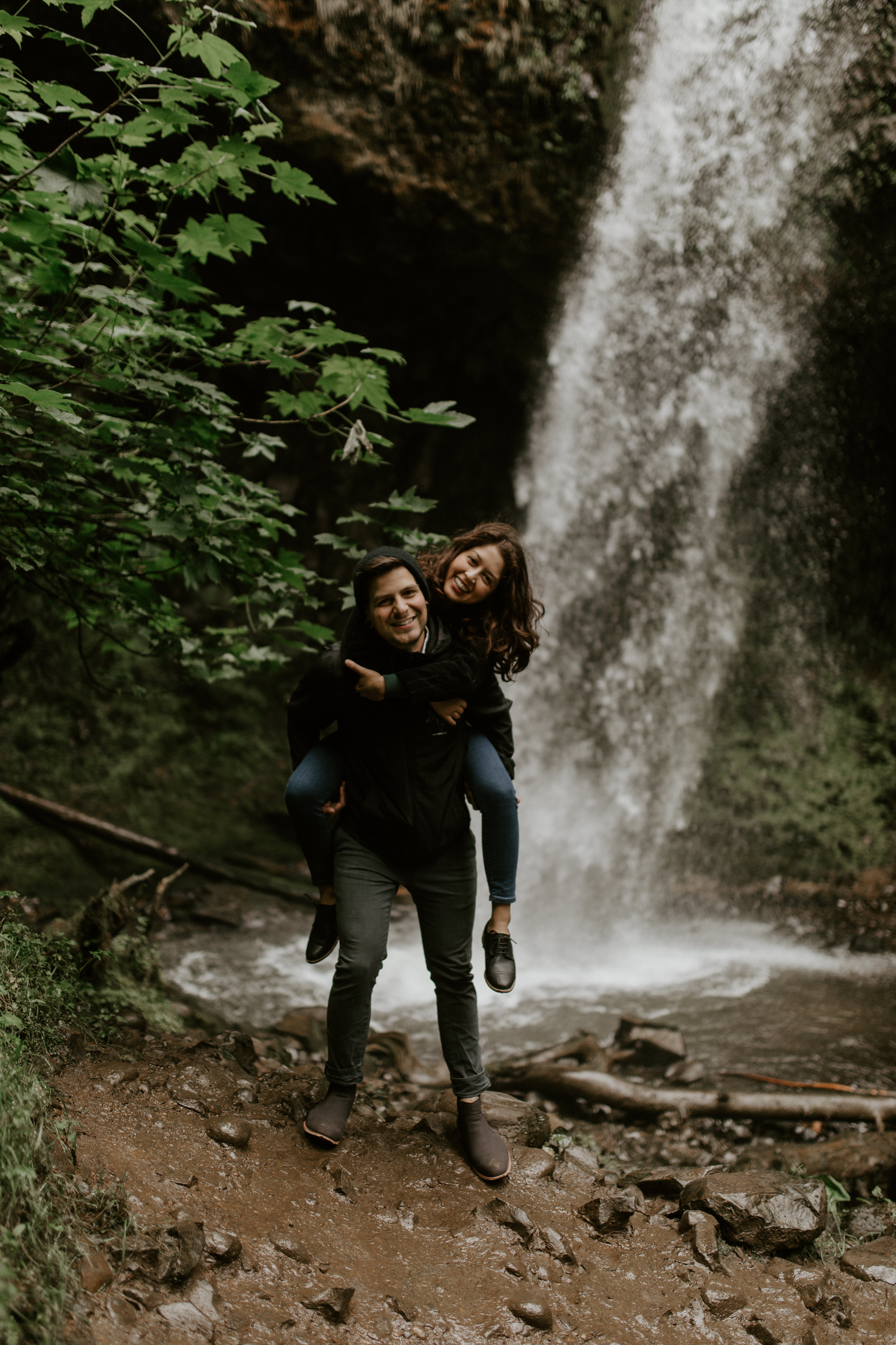 Chris gives Jasmine a piggy back ride in front of the upper falls of Latourell at the Columbia River Gorge in Oregon for her Oregon Adventure. Adventure photography in Portland Oregon by Sienna Plus Josh.
