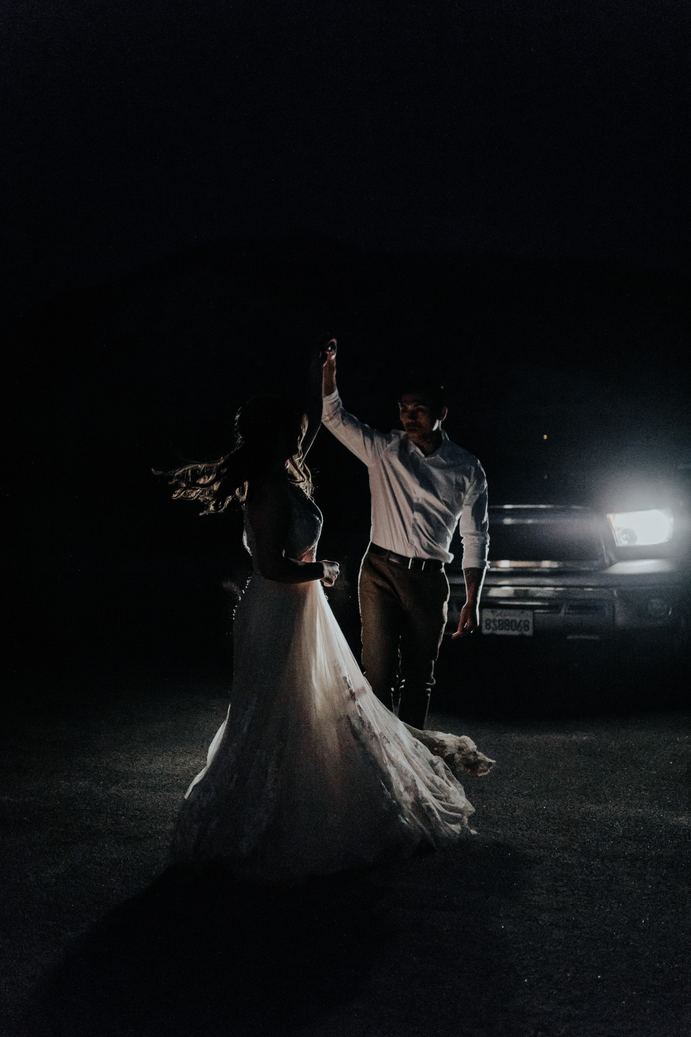 Zack spins Shelby in front of the headlights of their car in the dark of Joshua Tree National Park.