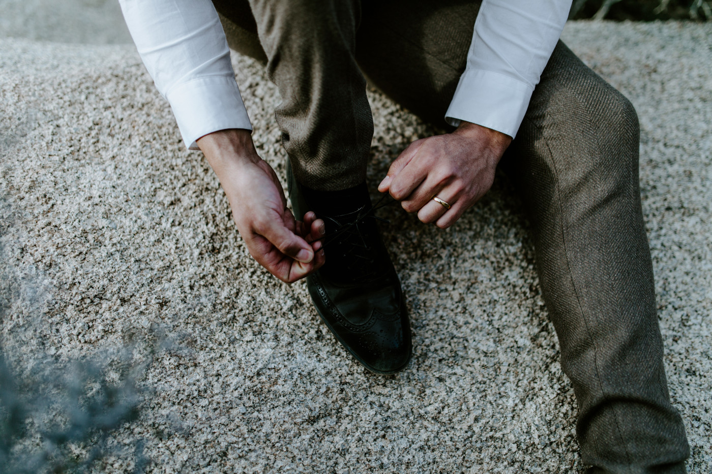 A close up of Zack tying his shoe while sitting on a rock in Joshua Tree National Park.