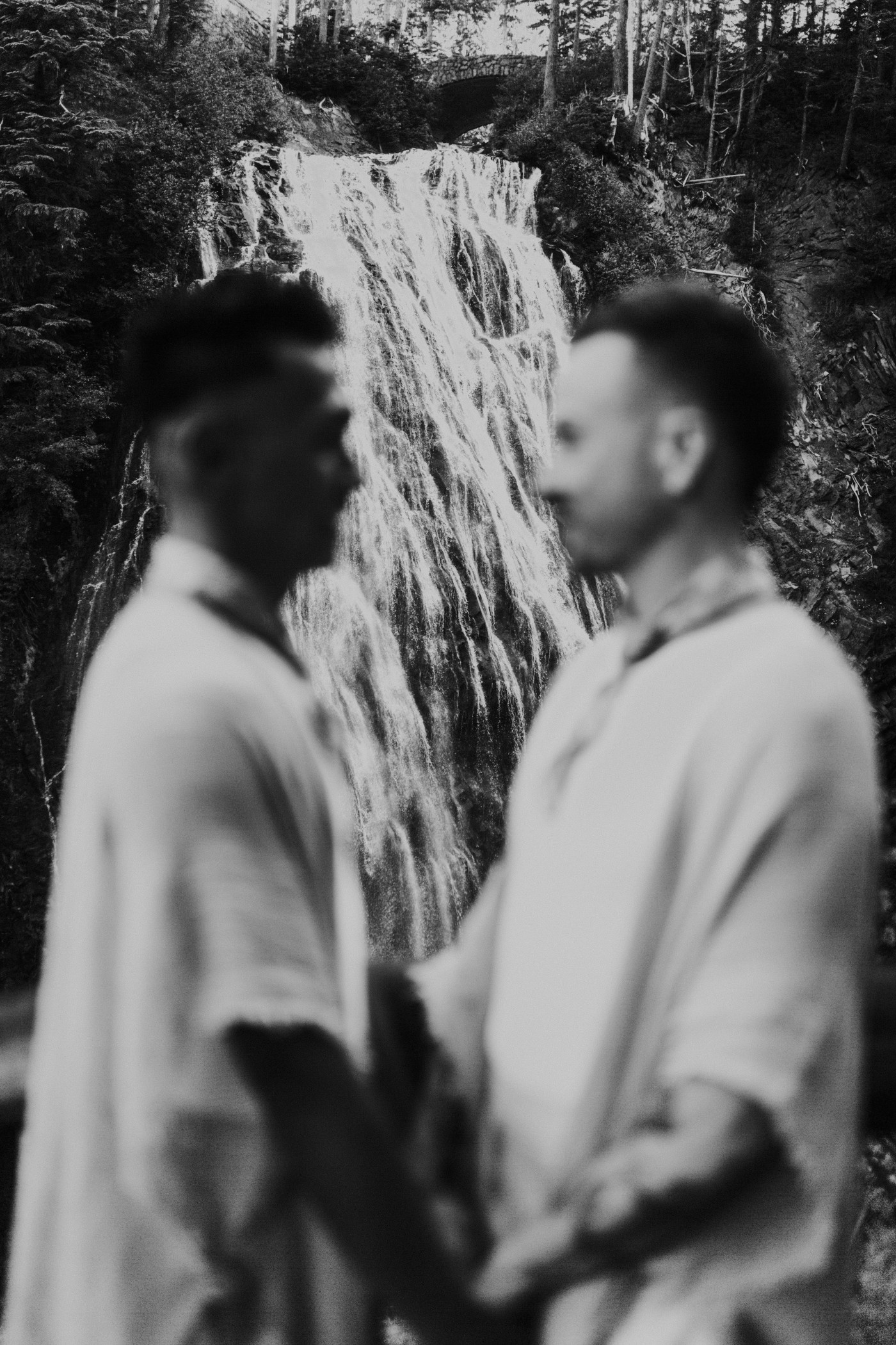 Brooks and Fred stand in front of a waterfall in Mount Rainier after their elopement.