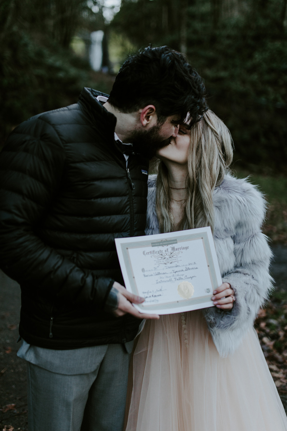 Boris and Tyanna kiss while holding their marriage certificate at Latourell Falls. Adventure elopement in the Columbia River Gorge by Sienna Plus Josh.